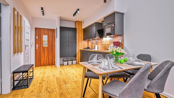 A compact dining area with a wooden table set for four, grey upholstered chairs, and a kitchen in the background with modern appliances. - Sun & Snow Karpatia (Karpacz)