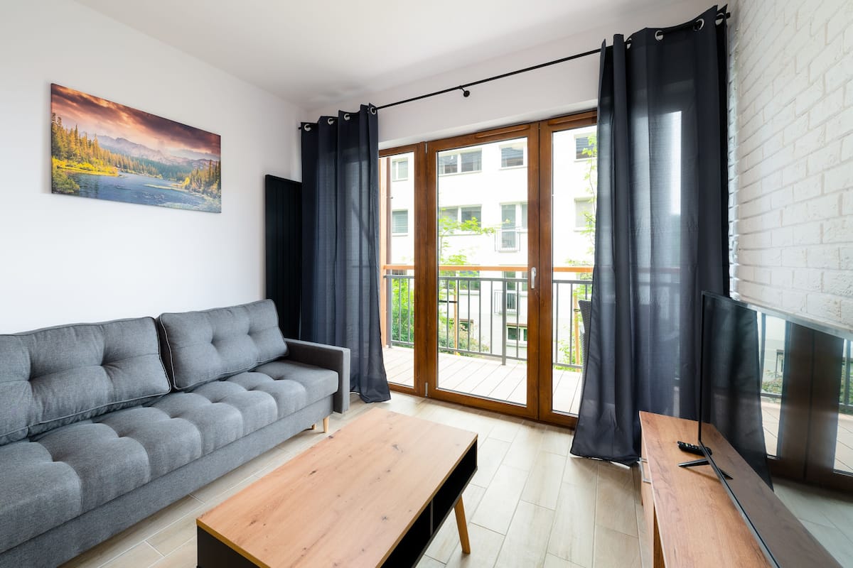 Un salon moderne avec un canapé gris, une table basse en bois et un tableau représentant un paysage.