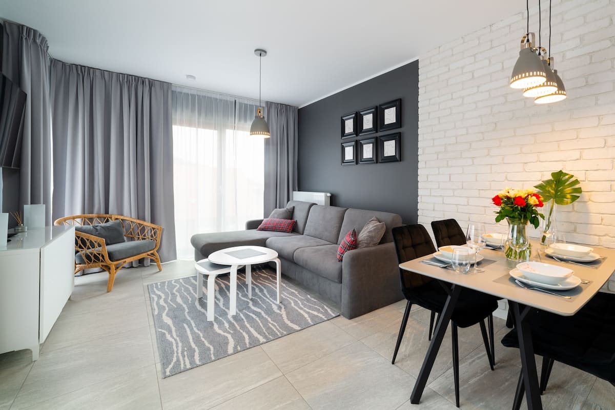 Un salon moderne avec un canapé gris, une table à manger dressée pour deux personnes et un mur en briques blanches.