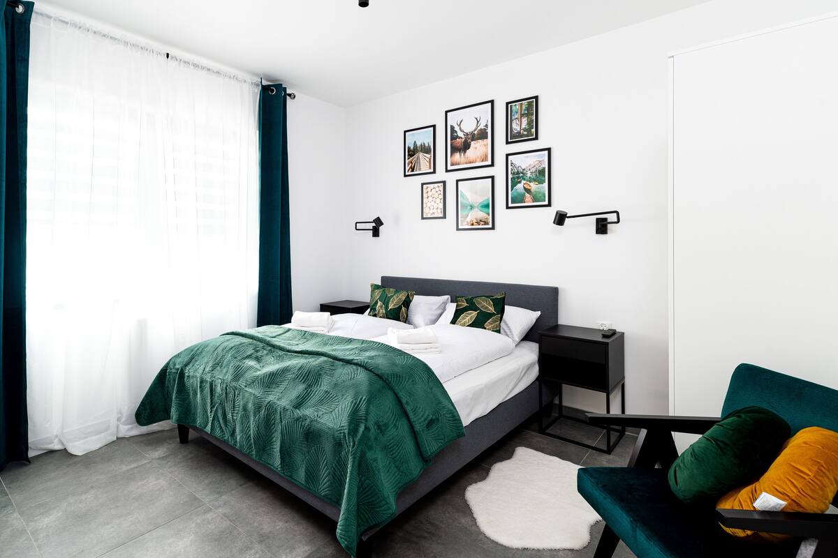 Une chambre d’hôtel moderne avec un lit bien fait, une petite table de chevet, une chaise et un téléviseur fixé au mur.