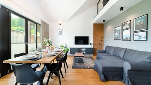 A modern living room with a grey sofa, wooden dining table, and a TV mounted on the wall.