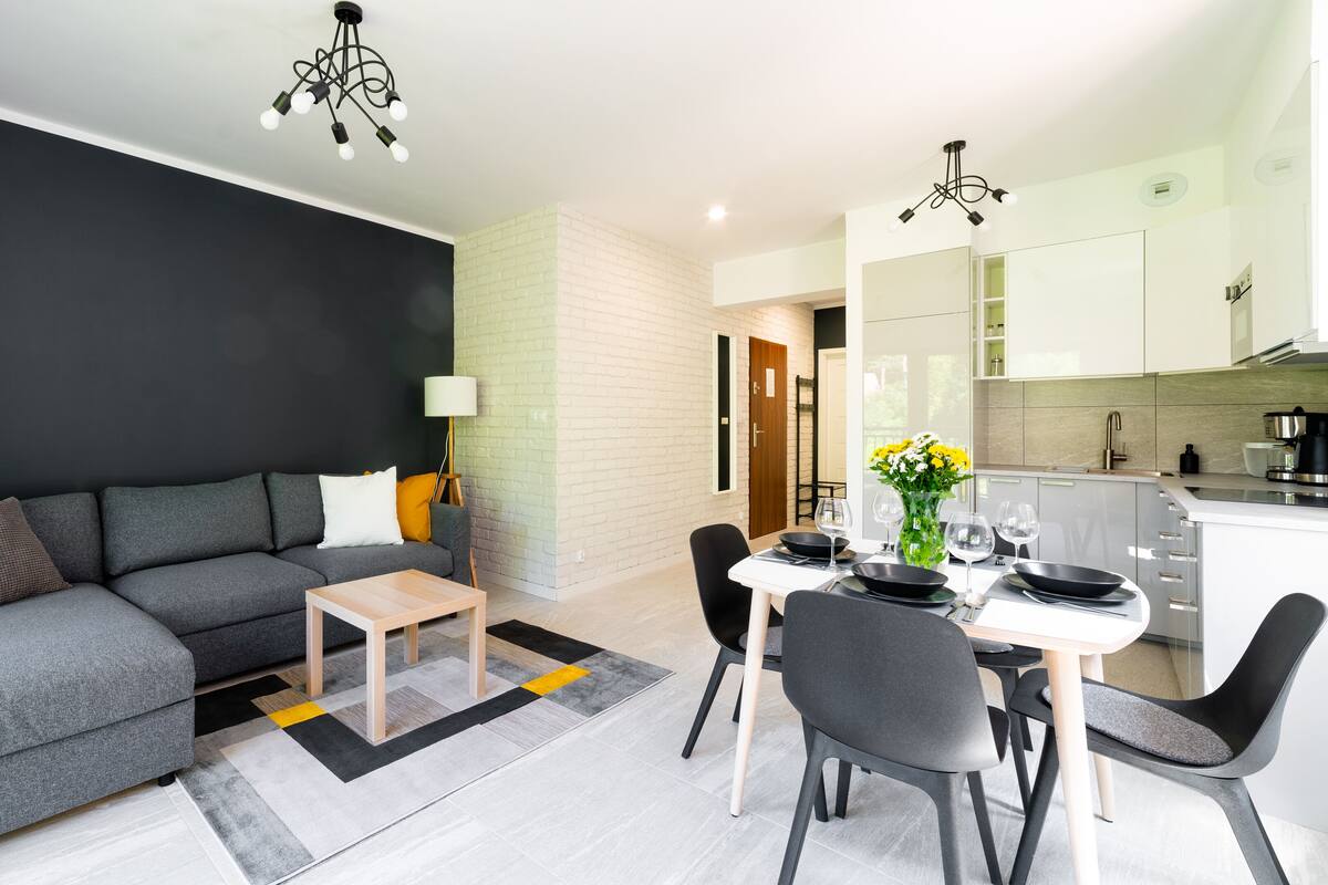 Un salon moderne avec un canapé gris, une petite table en bois et un coin repas comprenant une table blanche et des chaises noires.