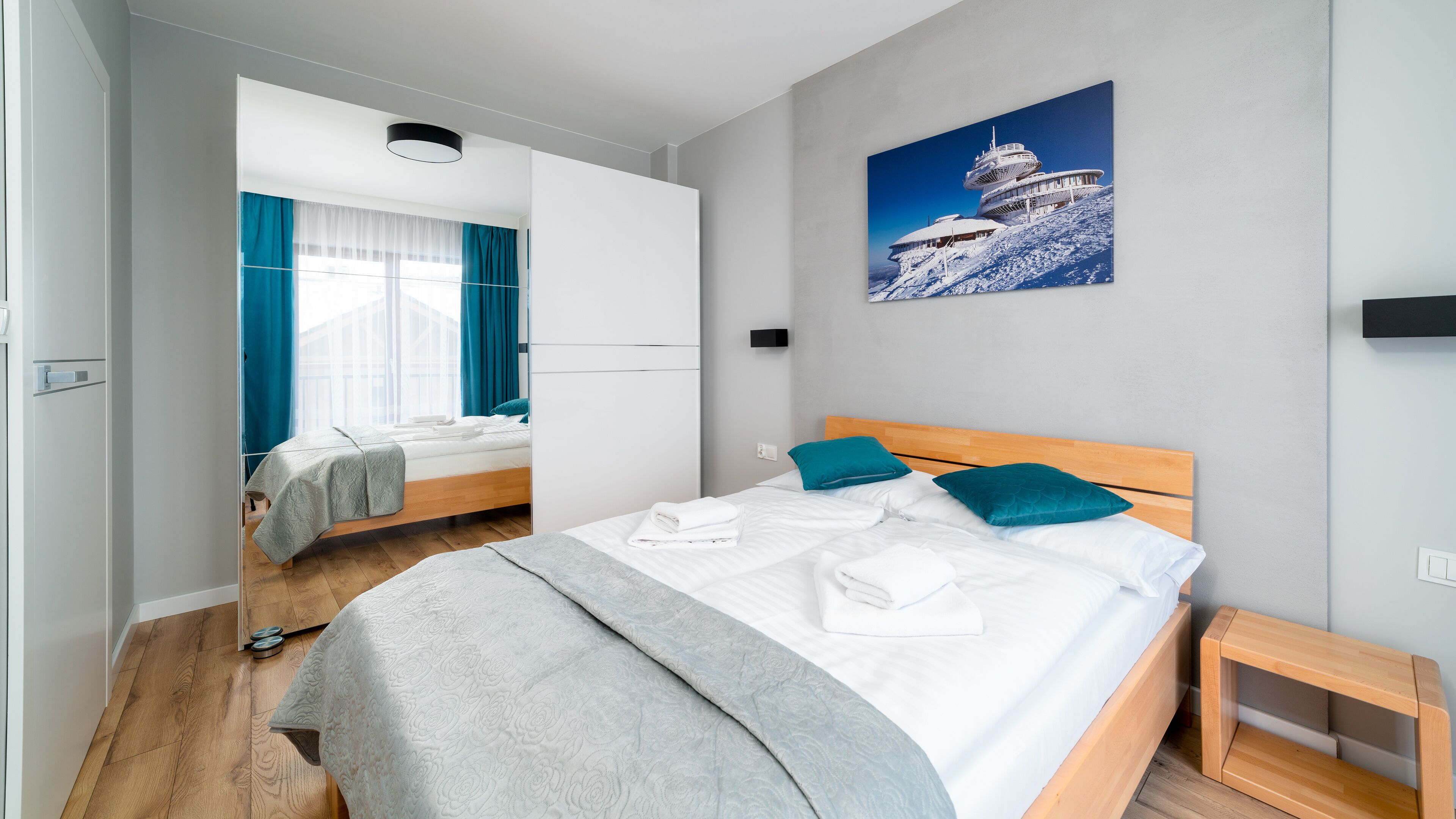 A modern hotel room with a large bed, a wooden headboard, and a view of a snowy mountain.