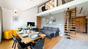 A modern living space with a dining area, sofa, and a staircase.