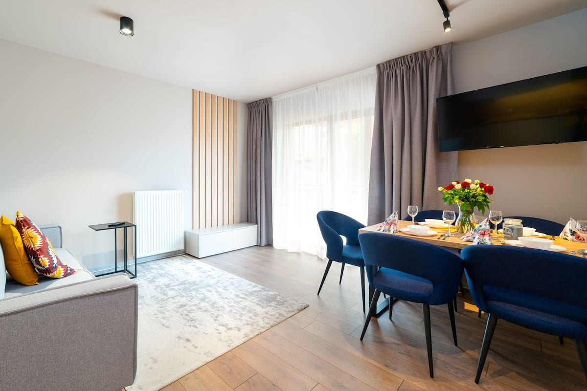 Un salon moderne avec un canapé, une table à manger pour deux personnes et un téléviseur à écran plat fixé au mur.
