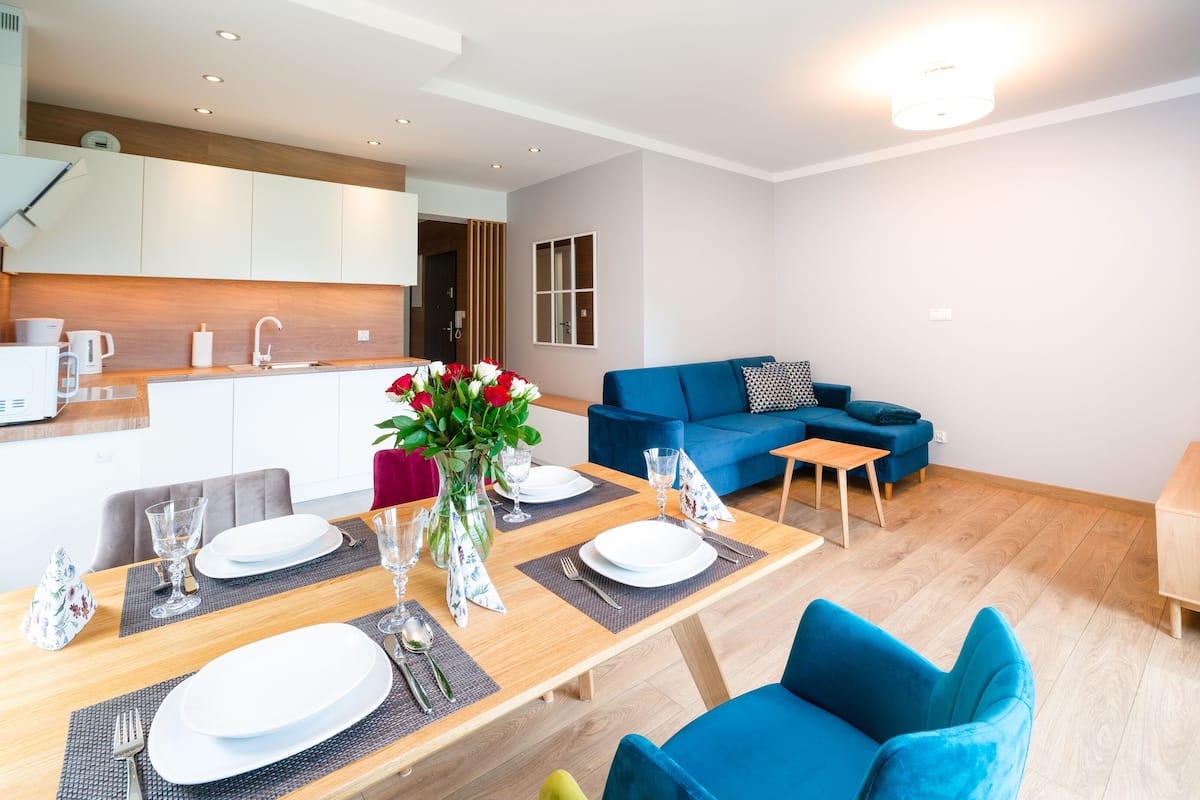 Un appartement moderne comprenant un coin repas, un canapé bleu et un téléviseur posé sur un meuble en bois.