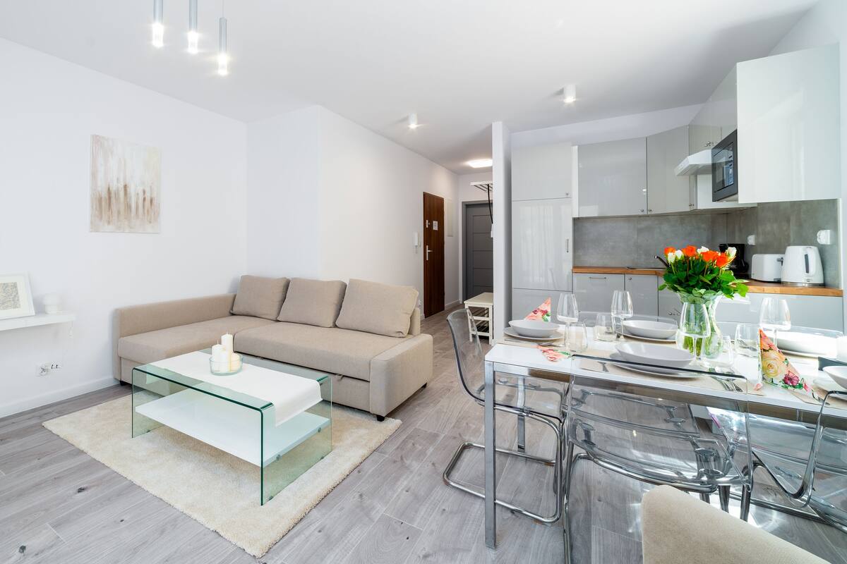 Un salon moderne avec une table basse en verre, un canapé beige et un coin repas comprenant une table et des chaises en verre.