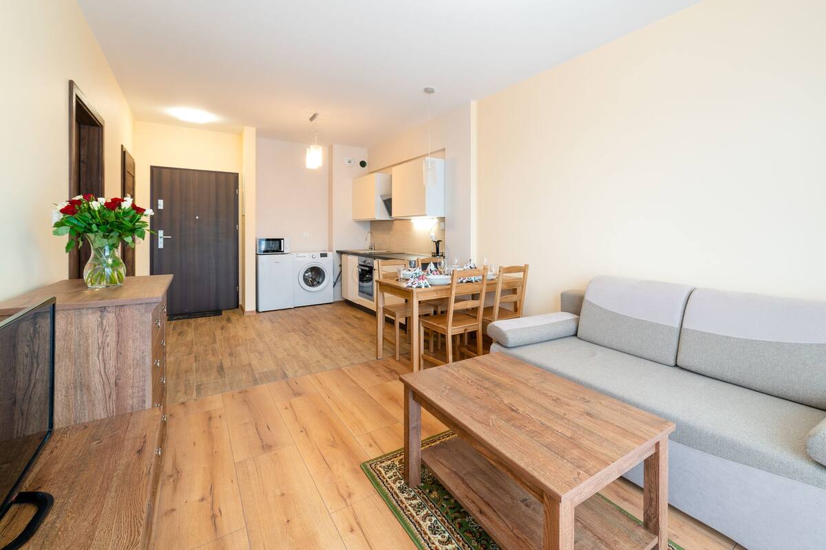 Un espace de vie compact comprenant un coin repas, un canapé, une table en bois et un lave-linge.