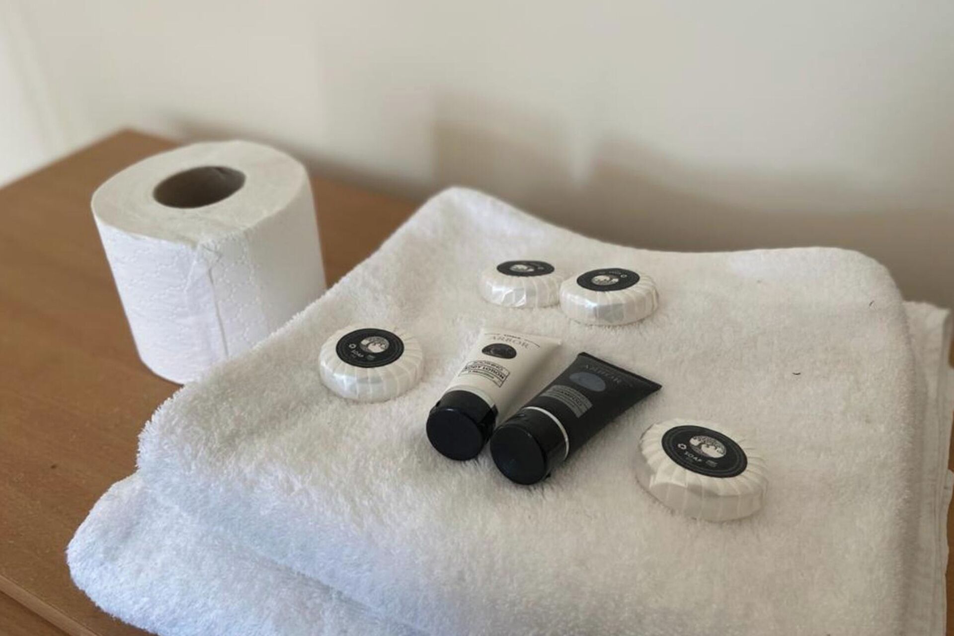 A bathroom with a white towel, a roll of toilet paper, and several toiletries on a white towel.