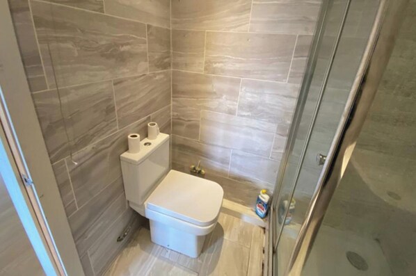 A small bathroom with a toilet, a shower, and a glass door. - Cozy Apartment Retreat in High Wycombe (High Wycombe)
