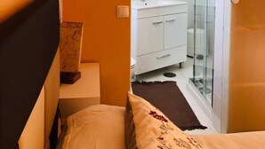 Ein Schlafzimmer mit einem Bett, einem Nachttisch und einer Tür zu einem Badezimmer mit Dusche und Toilette.