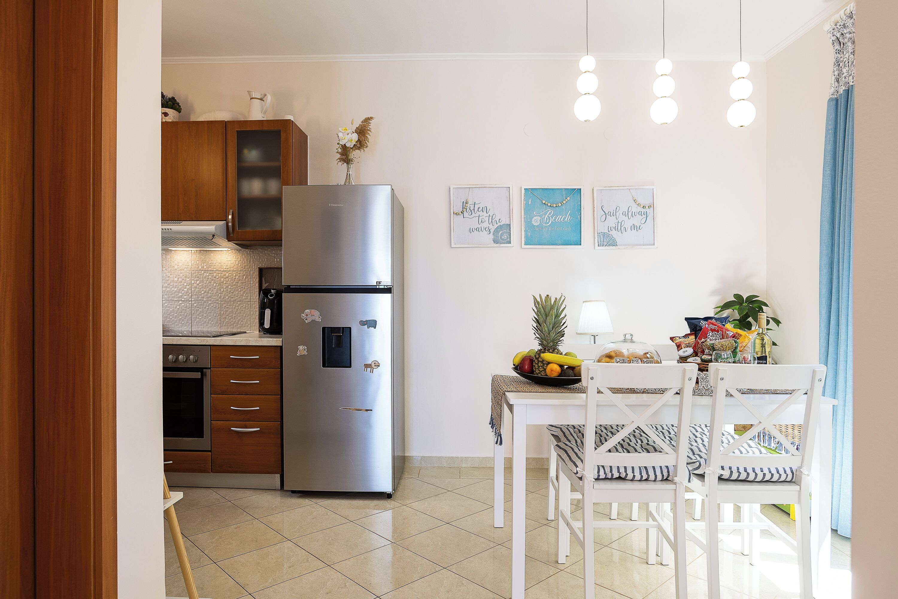 Een moderne keuken met een roestvrijstalen koelkast, houten kasten, een eettafel met stoelen en wanddecoratie.