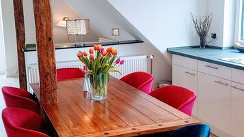 Een eetruimte met een houten tafel, rode en blauwe stoelen en een vaas tulpen.
