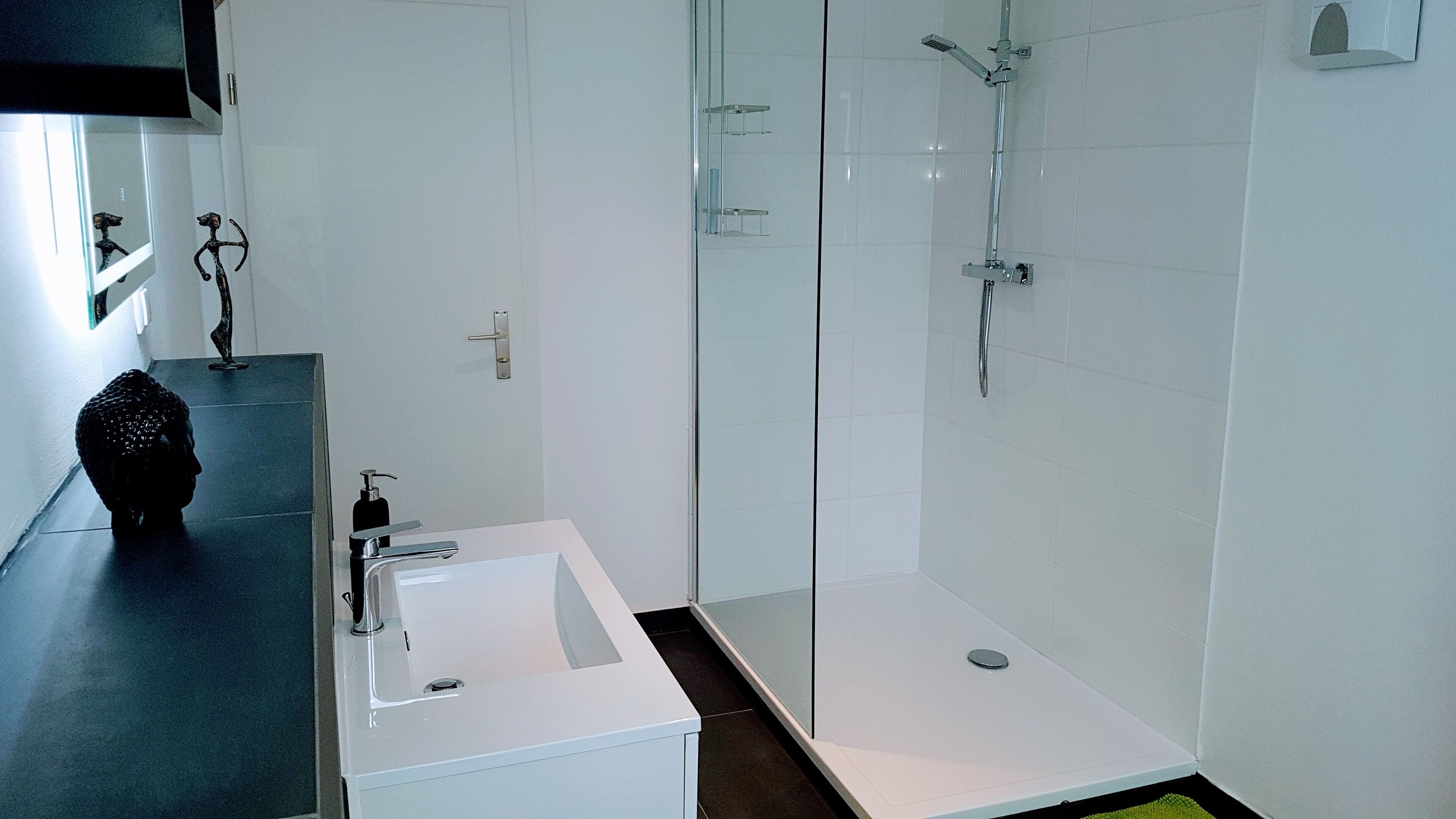 Un baño moderno con un lavabo blanco, una cabina de ducha de vidrio y una encimera negra.