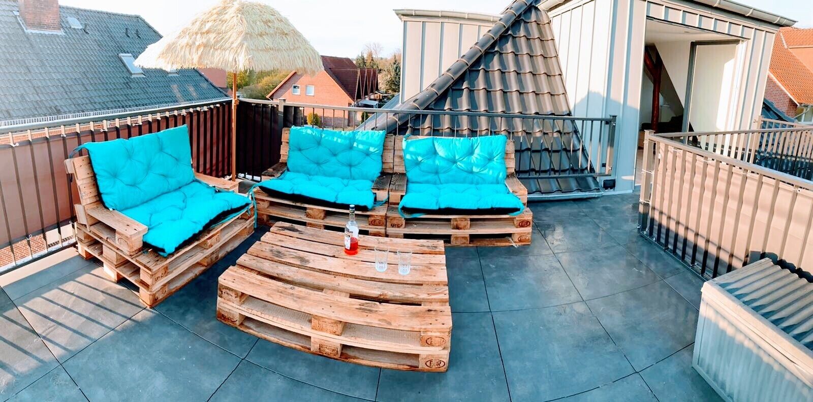 Une terrasse sur le toit, dotée de mobilier en bois et d’un parasol en chaume.