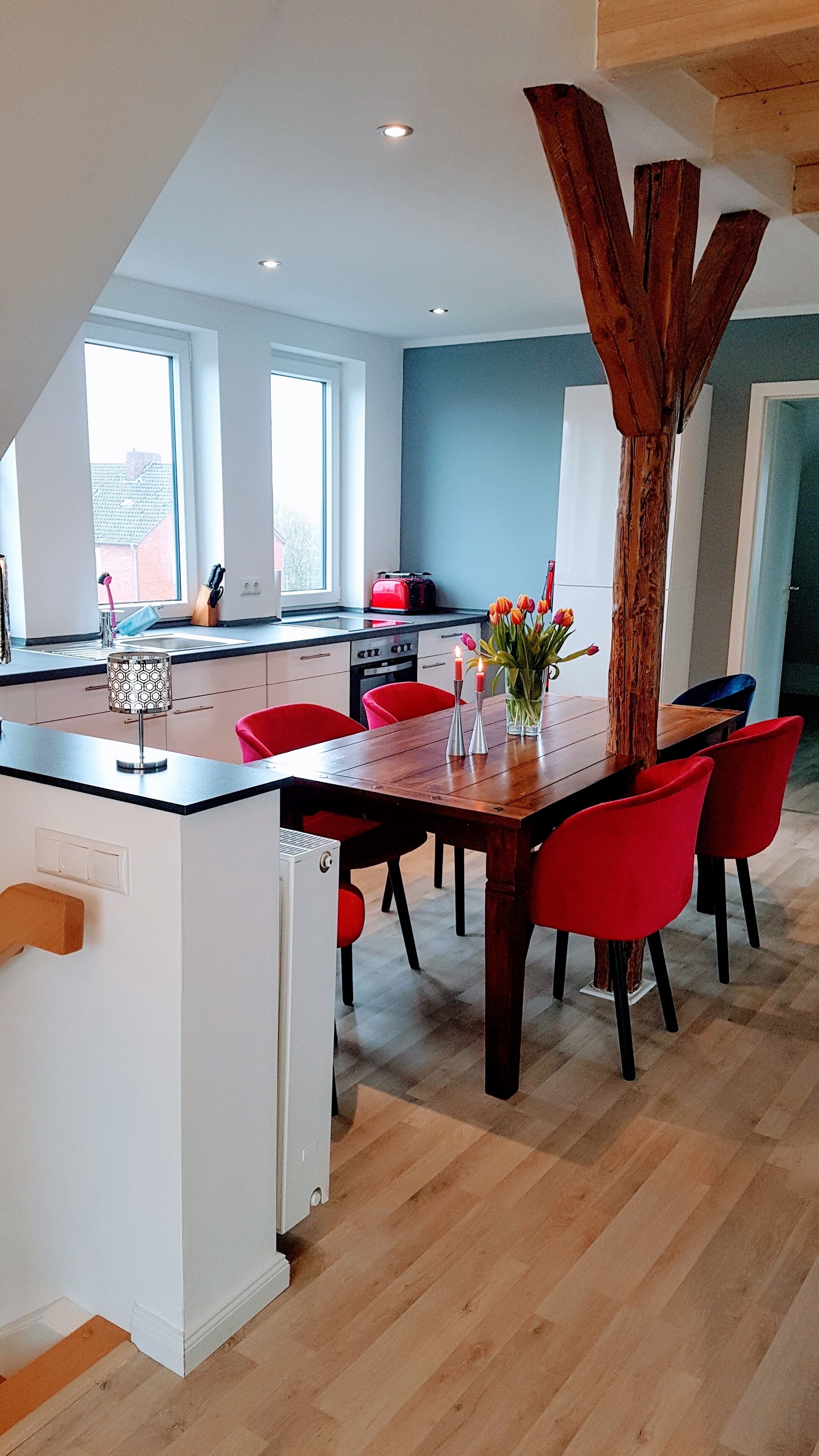 Una cocina moderna con una isla central, sillas rojas y un detalle de madera.