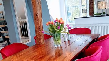 Un comedor con una mesa de madera, sillas rojas y azules, y un florero con flores.