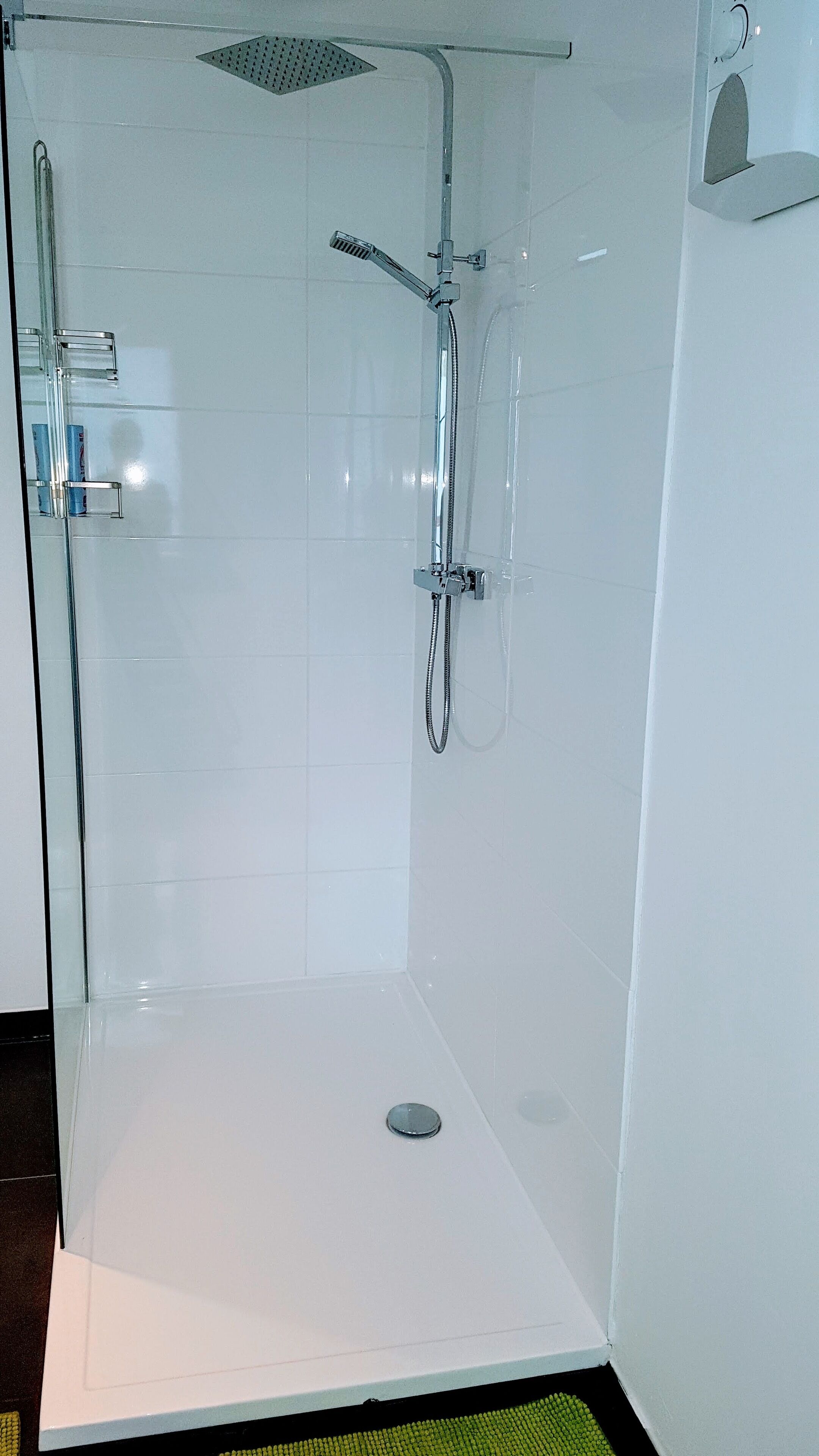 A glass-enclosed shower with a handheld showerhead and a wall-mounted faucet.