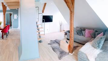 A modern interior with a dining area, a living room with a sofa and a TV, and a staircase.