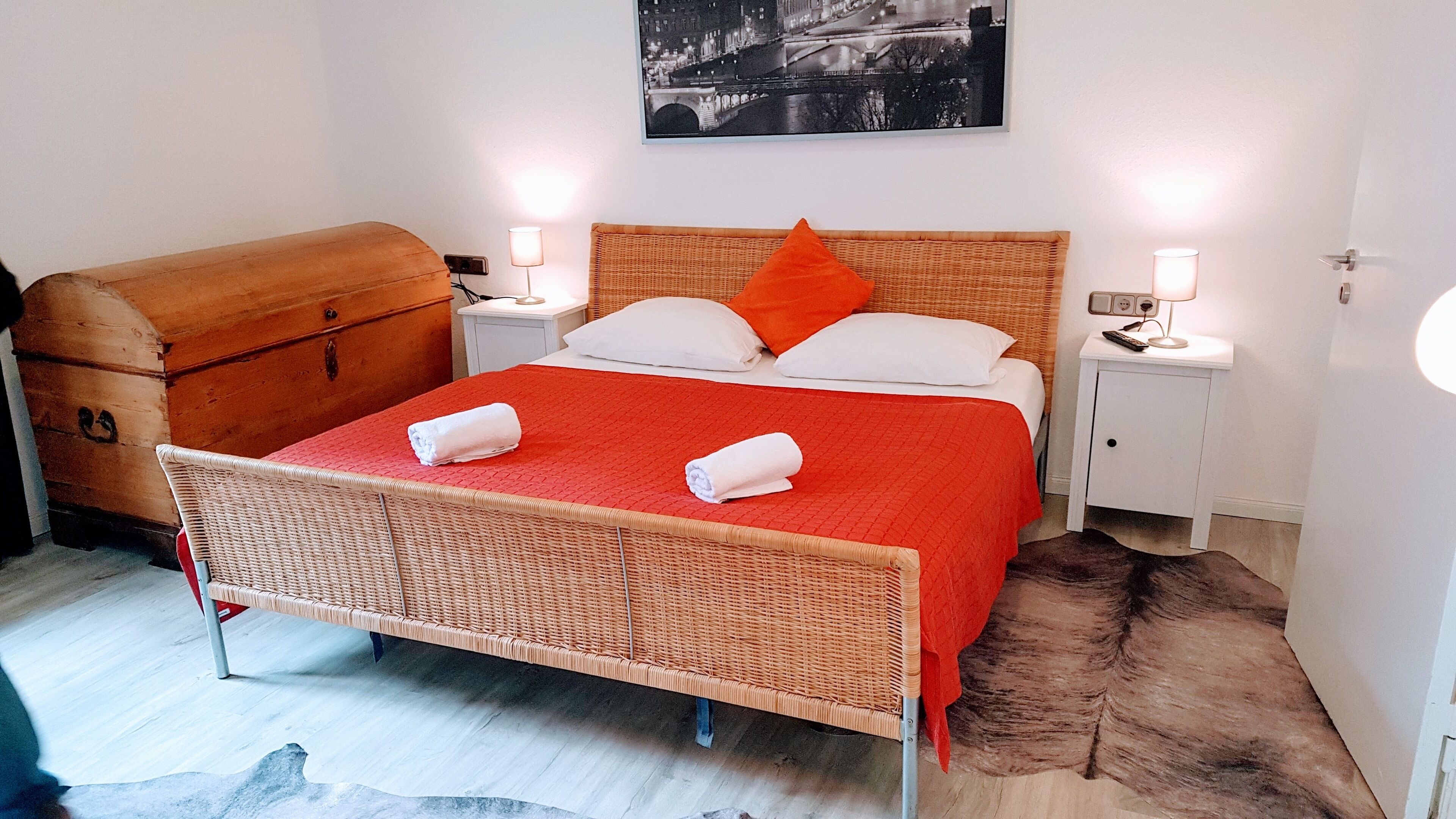 A room with a bed, a wooden chest, two bedside lamps, and a framed picture on the wall.