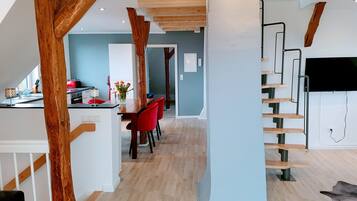 Eine moderne Küche mit Holzbalken, ein Essbereich mit roten Stühlen und eine Treppe mit Fernseher.
