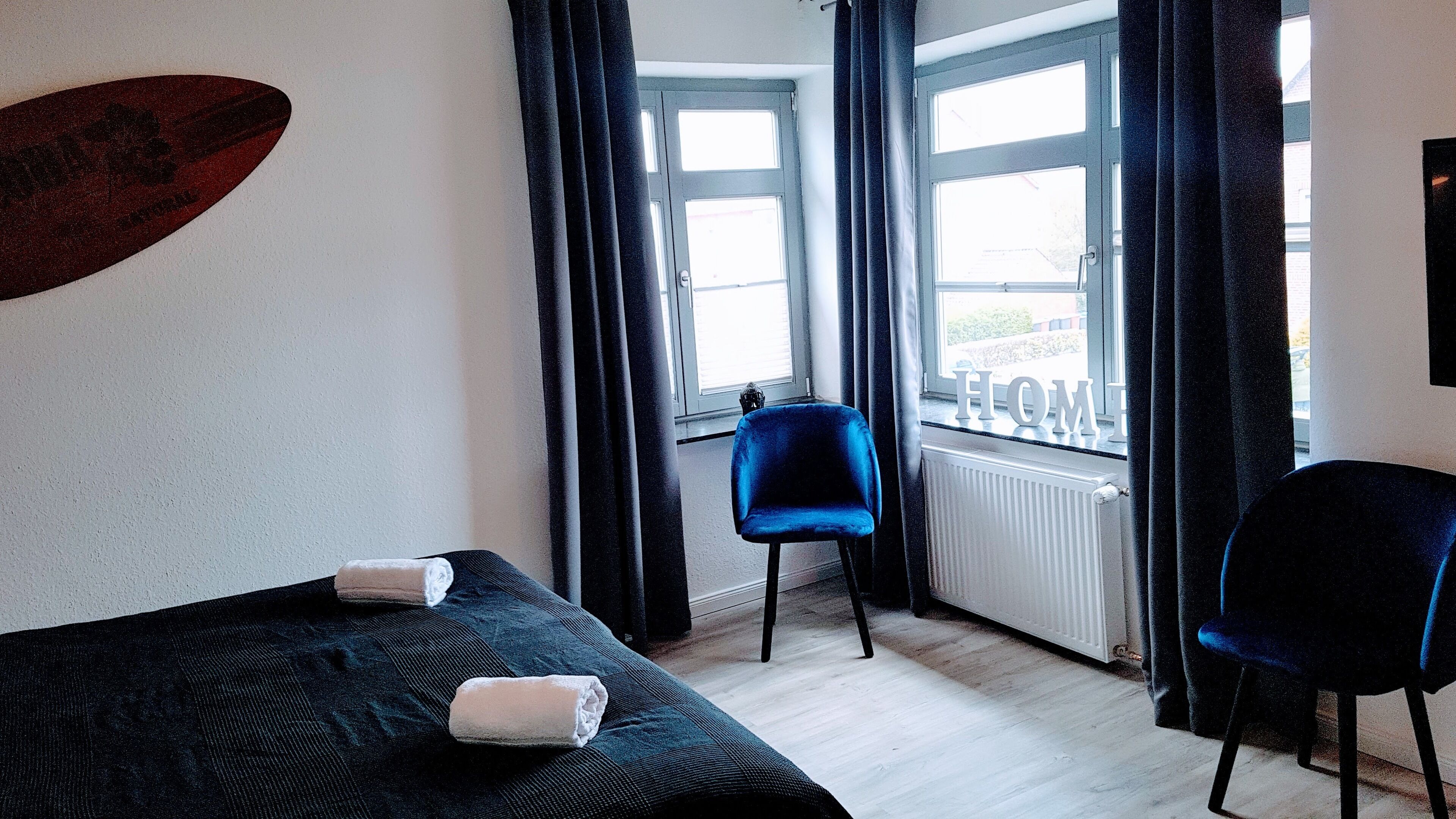 A bedroom with a bed, two chairs, a window with curtains, and a radiator.