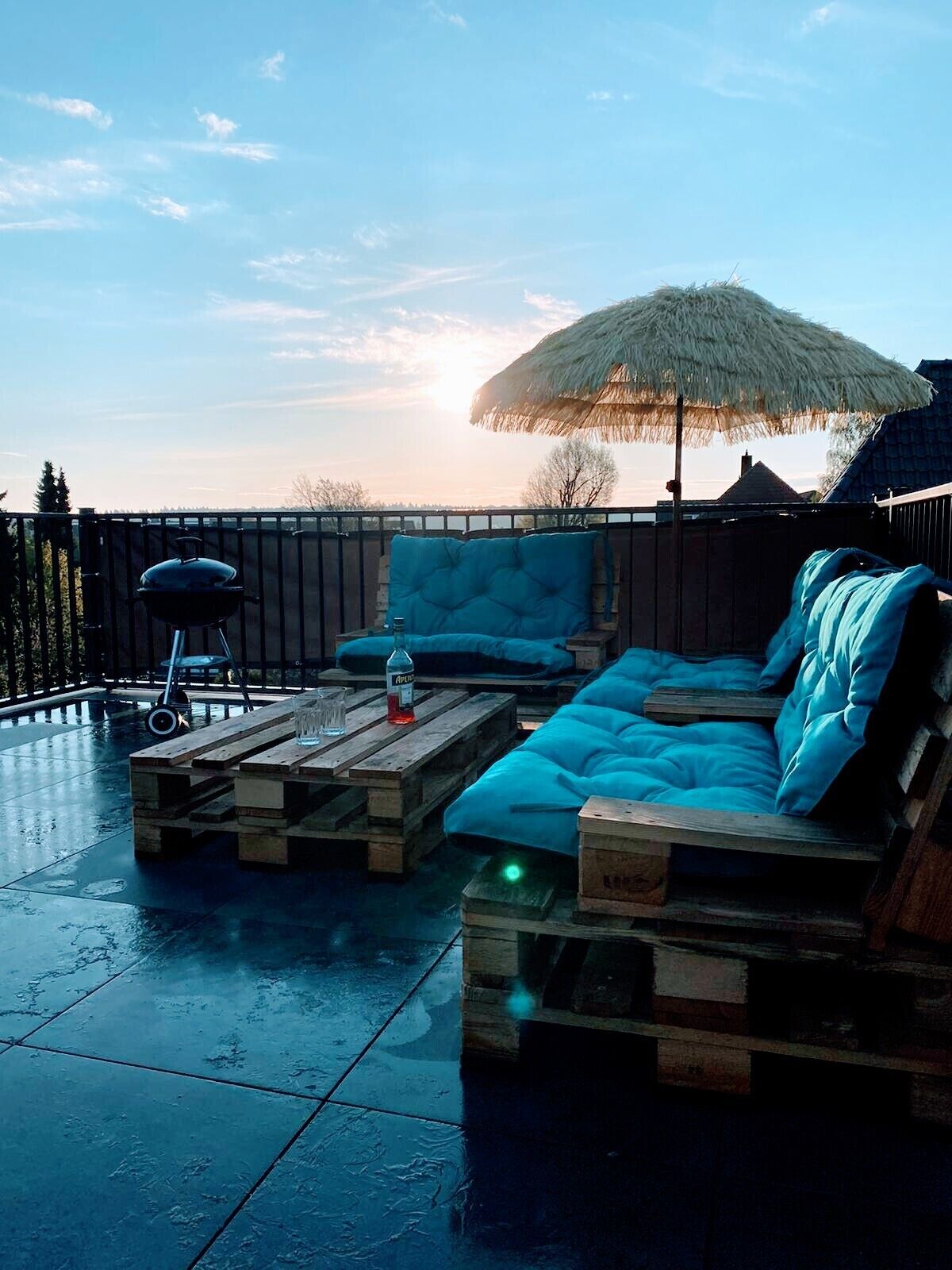 Un área de estar al aire libre con piscina, sombrilla de paja y una parrilla.
