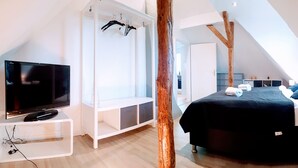 Ein modernes Schlafzimmer mit Fernseher, einem weißen Kleiderschrank, einem Bett mit blauen Kissen und einer Holzbalkenkonstruktion.