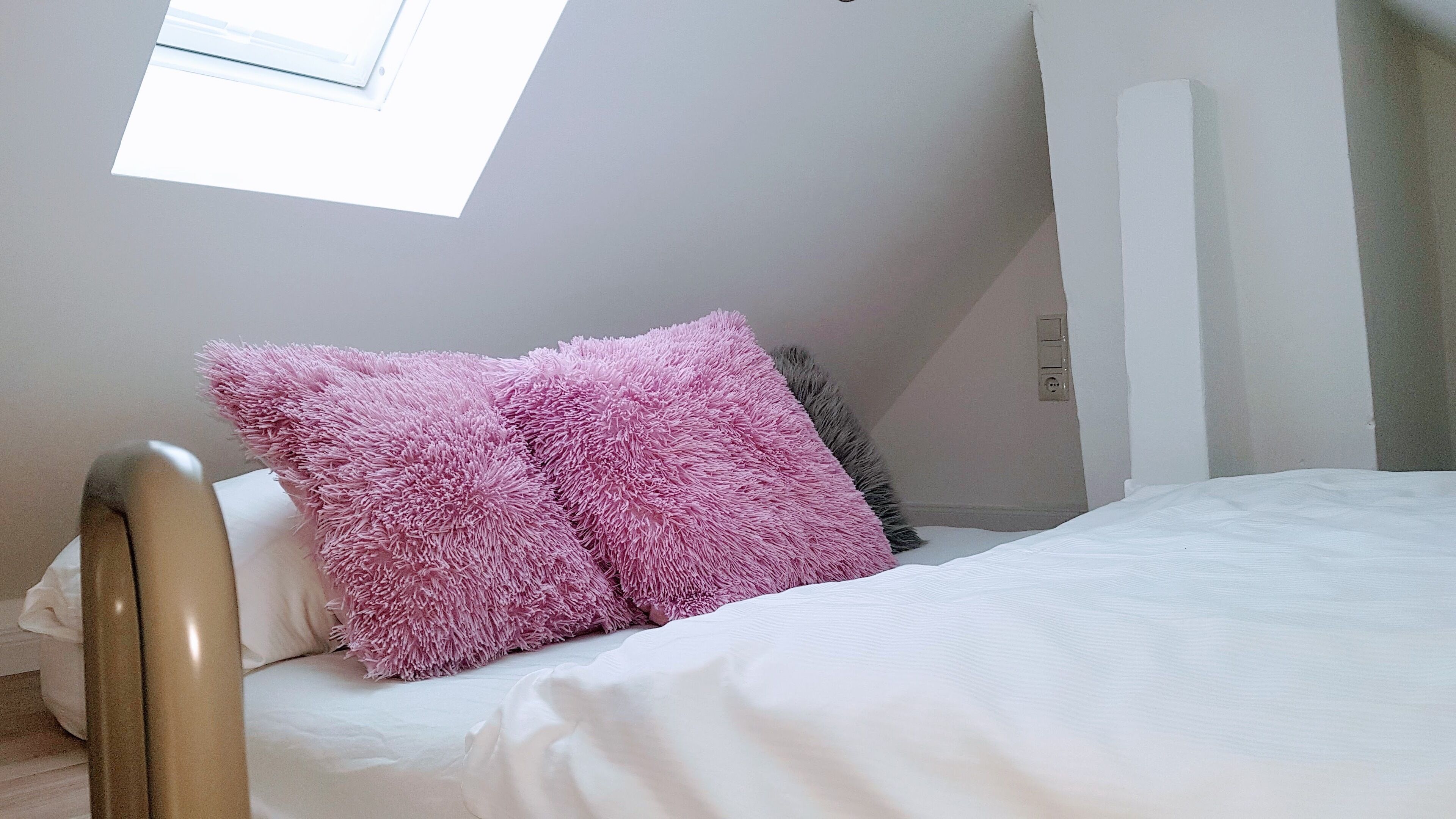 Un dormitorio con tragaluz, cama con ropa de cama blanca y dos almohadas rosadas y mullidas.