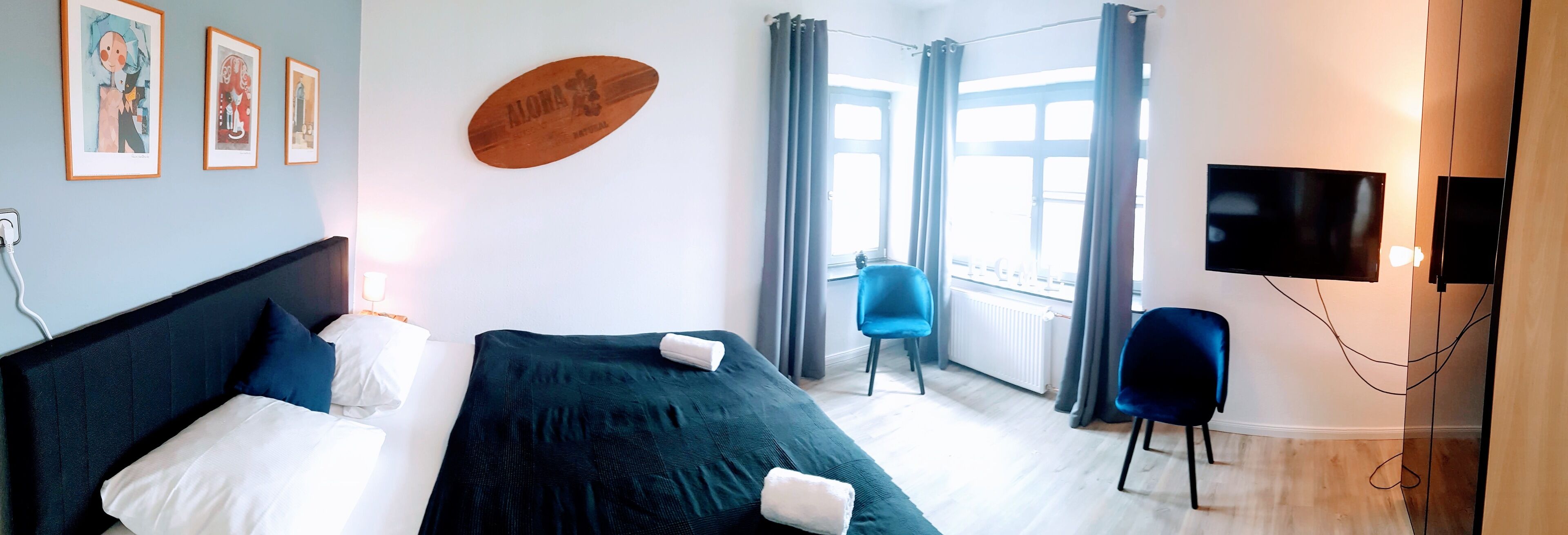 Ein Hotelzimmer mit Bett, Stuhl, Fernseher und einem Fenster mit Vorhängen.