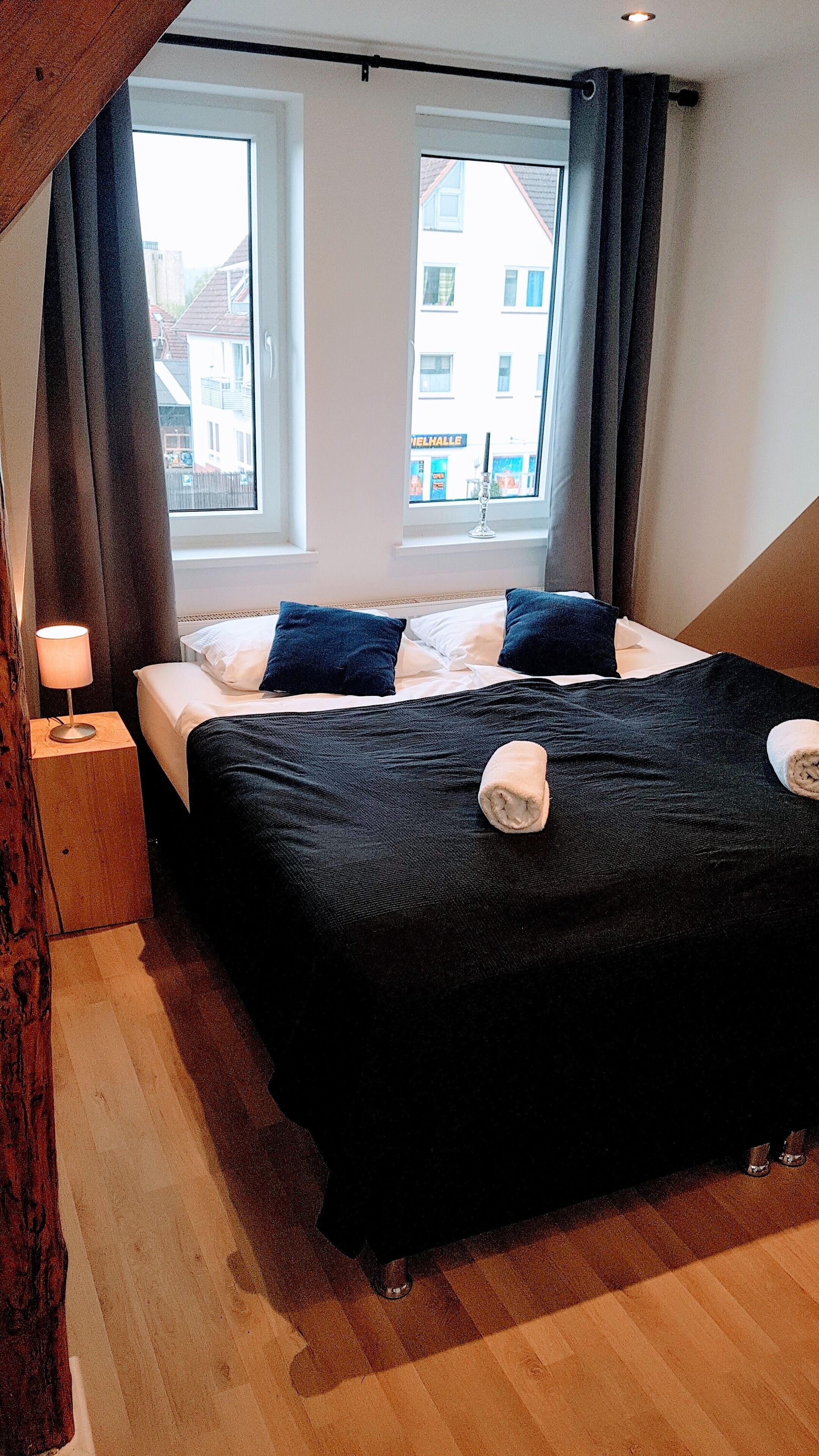 A bedroom with a bed, a nightstand, a lamp, and a window with curtains.