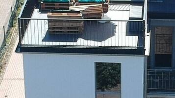 A modern building with a flat roof, a small balcony, and a window with a view of the street.