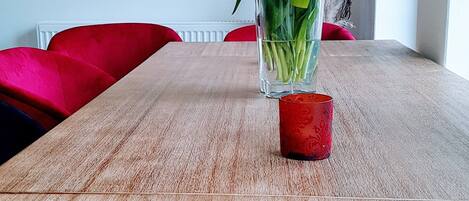 A dining table with a vase of tulips, a red candle, and a framed picture on the wall.