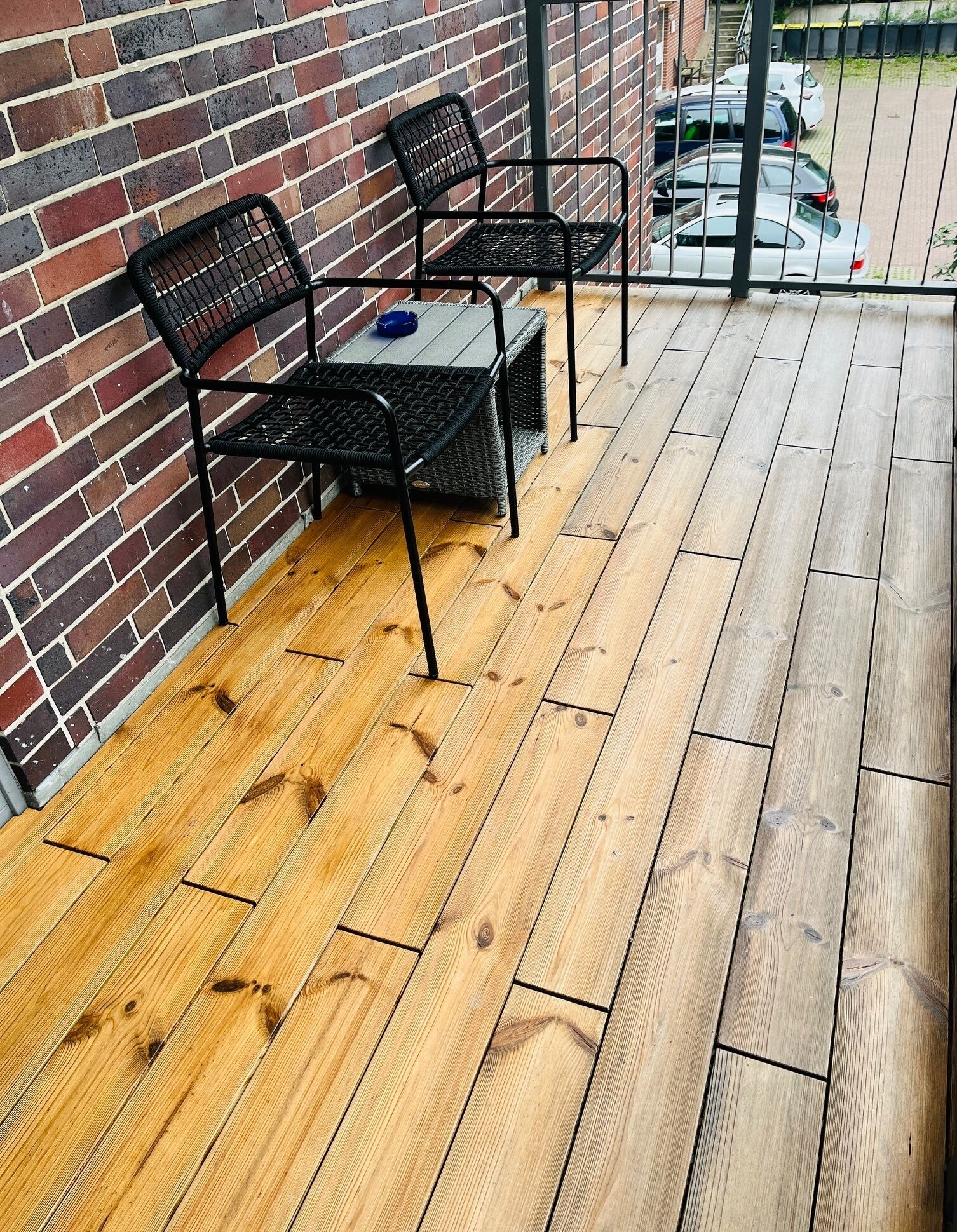 A wooden deck with two black metal chairs and a small table.