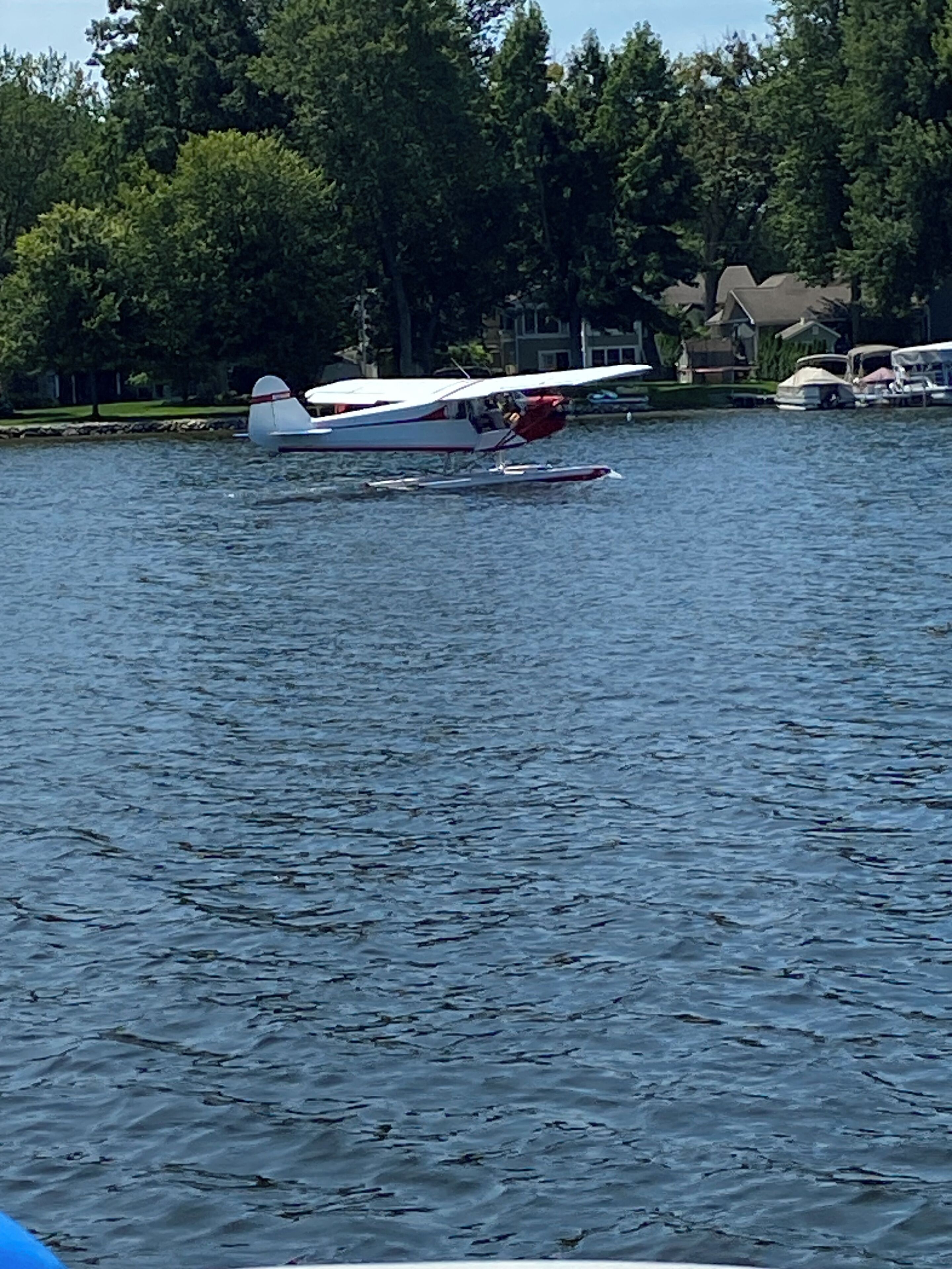 Un lago con un hidroavión blanco pequeño y un hidroavión rojo y blanco atracados cerca de la orilla.