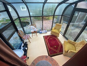 Een oranjerie met een rood geweven vloerkleed, twee gele fauteuils, een houten stoel en een pluchen speelgoed.