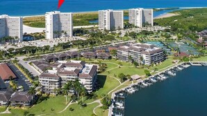 Vista aérea de un complejo hotelero frente al mar, con varias construcciones, un puerto deportivo y una playa.