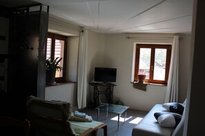 A living room with a sofa, a glass coffee table, a television, and a potted plant.