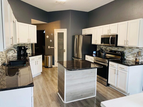 A modern kitchen with white cabinets, stainless steel appliances, and a central island. - Elegant single level with 4 BR 3 BA, private oasis featuring a heated salt pool (Navarre)