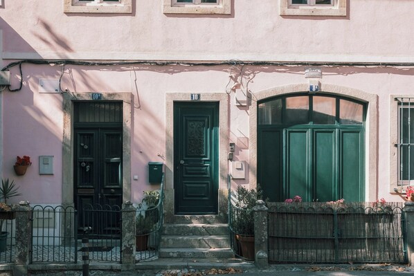 A pink building with three doors, a small porch, and a metal fence.