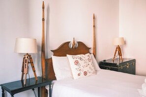 Un letto rifatto con cura, con una testiera in legno, due comodini con lampade e un cuscino floreale.