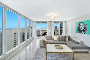 Relax in this stylish living room with a large sofa, coffee table, and floor-to-ceiling windows offering a city view.
