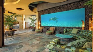 A spacious lobby with a large wall-mounted screen displaying a turtle, comfortable seating areas, and a stone wall. - Mana Kai 2BR across Kamaole III Beach, ocean views, summer deal (Kihei)