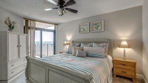 Un dormitorio con cama, mesitas de noche, ventilador de techo, armario y vistas al exterior.