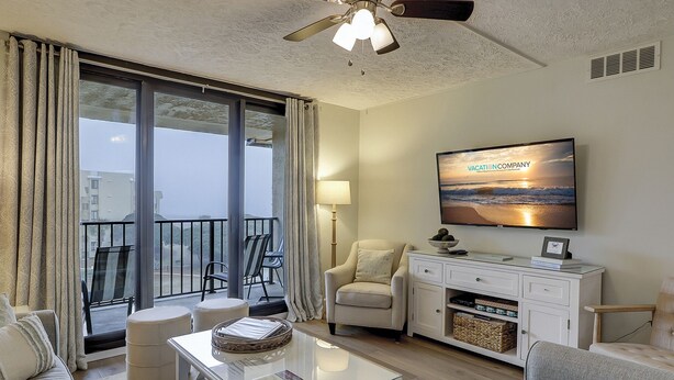 Ein Wohnzimmer mit Balkon, Deckenventilator, Flachbildfernseher und Sofa.