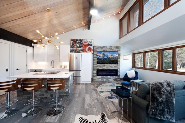 A modern kitchen with a central island, a dining area with bar stools, a fireplace, and a cozy seating area with a sofa and a chair. - Sunshine Suite | AC, Pool, Hot Tub, Golf & Ski (Durango)