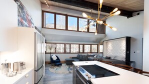 A modern kitchen with a central island, a dining area with a white table, and a cozy seating area with a blue chair and gray sofa. - Sunshine Suite | AC, Pool, Hot Tub, Golf & Ski (Durango)