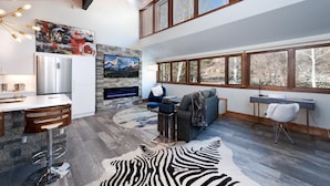 A spacious living area with a stone fireplace, a large TV, and a zebra rug. - Sunshine Suite | AC, Pool, Hot Tub, Golf & Ski (Durango)