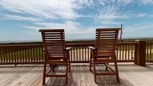 Zwei Holzstühle auf einer Holzterrasse mit Blick auf das Meer.