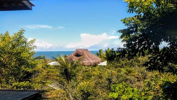 A tropical landscape with a thatched-roof hut, dense greenery, and a view of the ocean.
